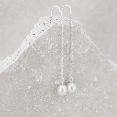 oval cream pearls on a silver threader earring , shown against grey stone background